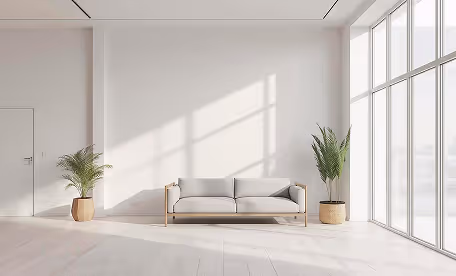 Minimalist living room with a light gray sofa between two potted plants and large floor-to-ceiling windows letting in natural light.
