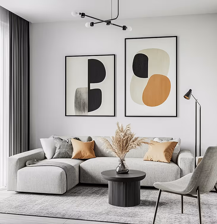 Modern living room with a light gray sectional sofa, two abstract framed artworks, a black round coffee table with a vase of dried pampas grass, a gray chair, and a floor lamp.