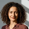 Smiling woman with curly hair wearing a brown blouse against a light background.