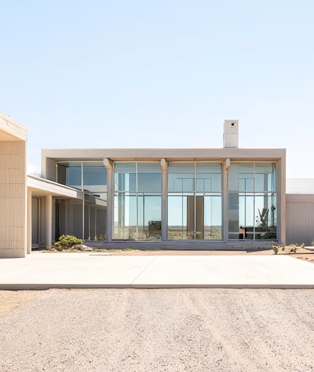 Modern building with large glass windows reflecting the landscape, set in a desert-like area.